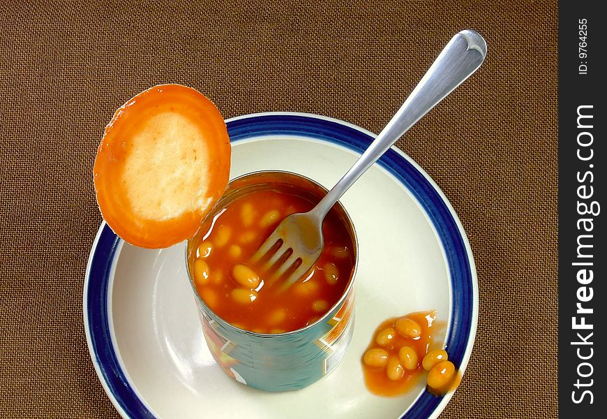 An opened tin of baked beans, with fork, sitting on a plate. An opened tin of baked beans, with fork, sitting on a plate.