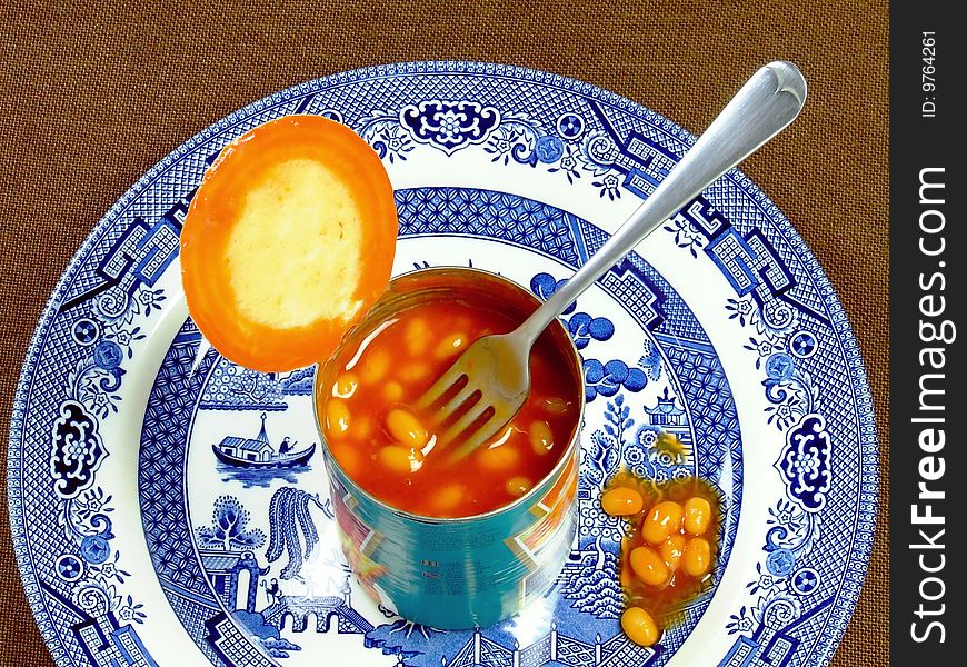 An opened tin of baked beans, with fork, sitting on a dinner plate. An opened tin of baked beans, with fork, sitting on a dinner plate.