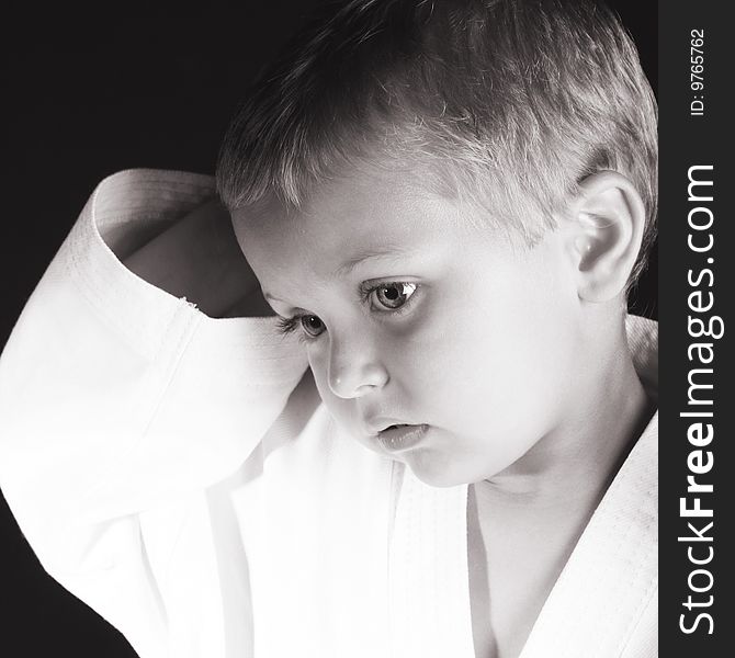 Young boy wearing his karate uniform on a black background. Young boy wearing his karate uniform on a black background