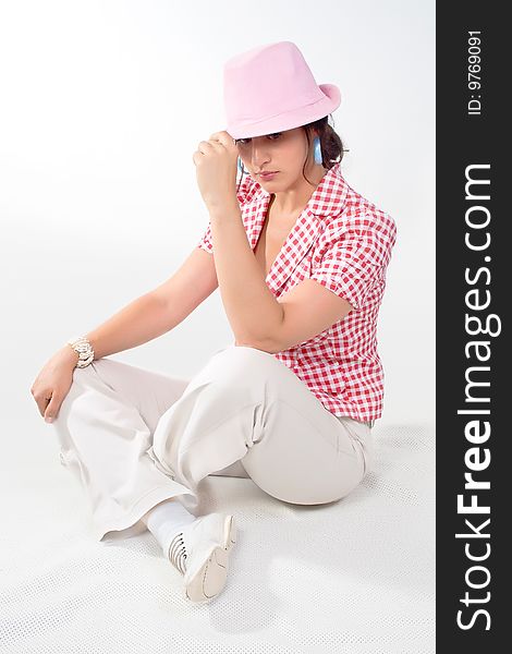A nice young woman in a hat sitting with legs crossed, on white background. A nice young woman in a hat sitting with legs crossed, on white background