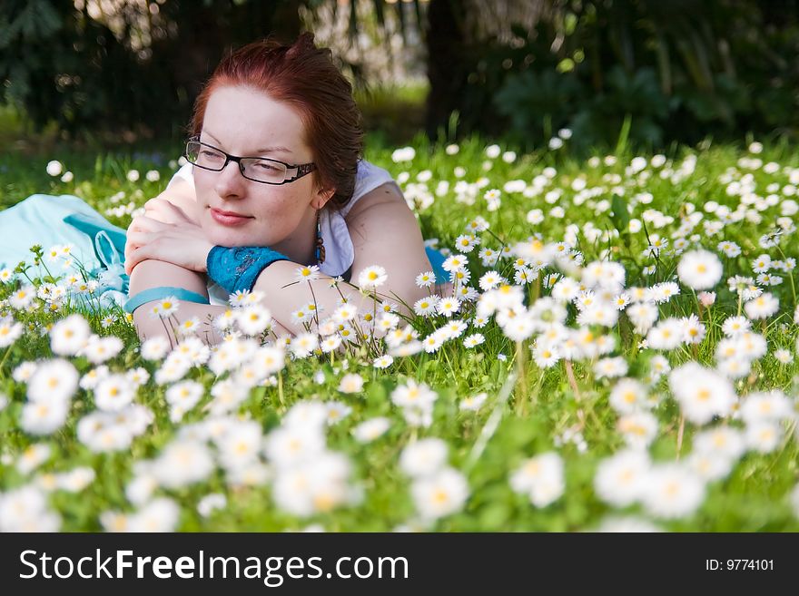 Young woman with glasses laying on grass in park full of small white flowers. Young woman with glasses laying on grass in park full of small white flowers.