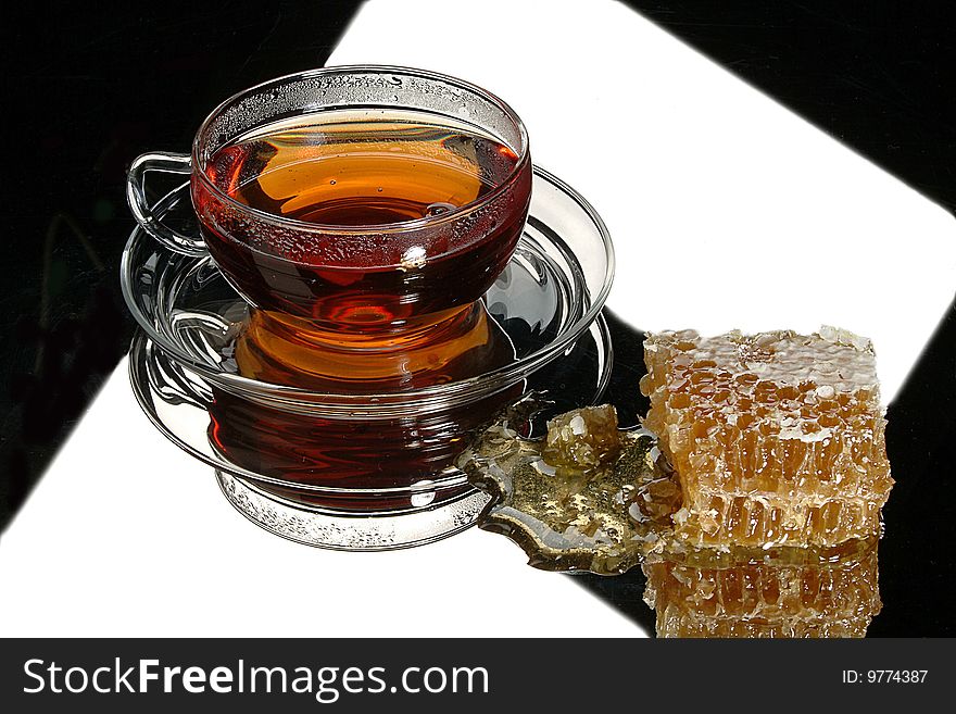 Glass cup of tea and a piece of honey comb on a black glass. Glass cup of tea and a piece of honey comb on a black glass