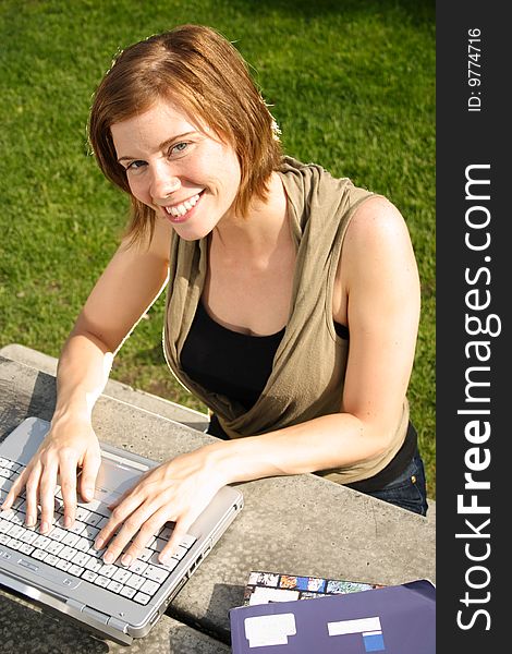 A female student typing on her laptop computer at a picnic table on campus. A female student typing on her laptop computer at a picnic table on campus