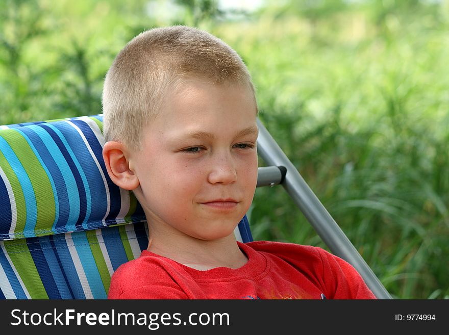 The boy in a chaise lounge smiles having a rest on the nature. The boy in a chaise lounge smiles having a rest on the nature