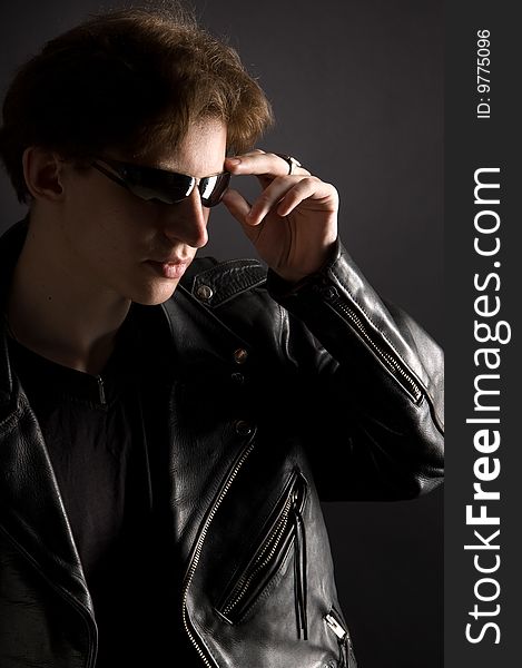 A young man in leather jacket and sunglasses, black background