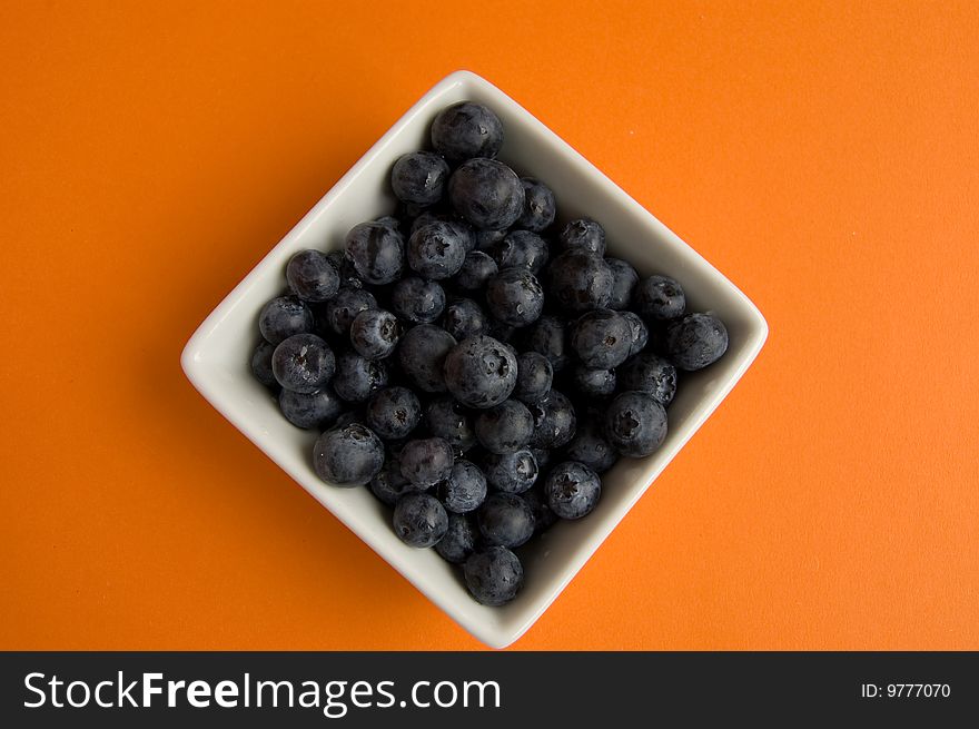 Fresh blueberries in square white bowl on orange background