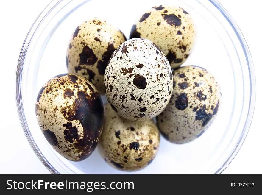 Overhead shot of quail eggs in glass bowl on white background