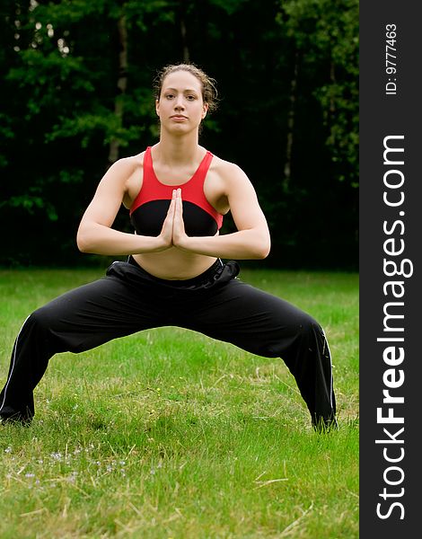 Practising Yoga In A Green Field With Trees