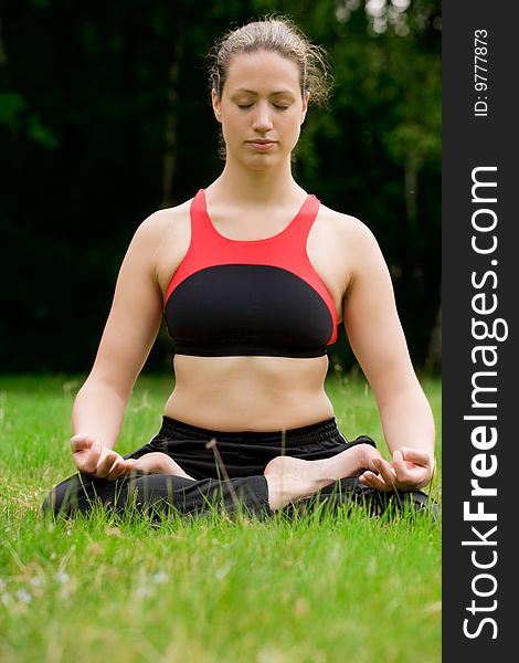 Young adult woman practising yoga on a field surrounded by trees. Young adult woman practising yoga on a field surrounded by trees