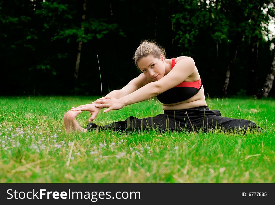 Practising yoga in a green field with trees