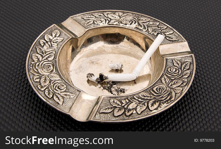 Metall ashtray with cigarette on the black background