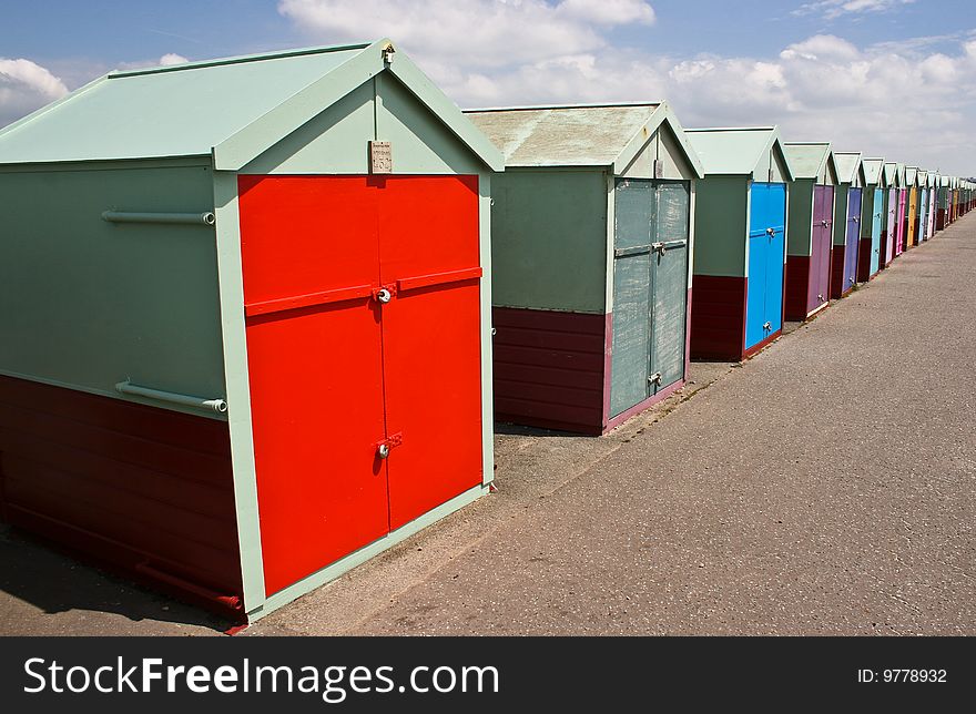 A long colourful row of beach huts at the seaside in Brighton, england with aback drop of blue sky and clouds. A long colourful row of beach huts at the seaside in Brighton, england with aback drop of blue sky and clouds