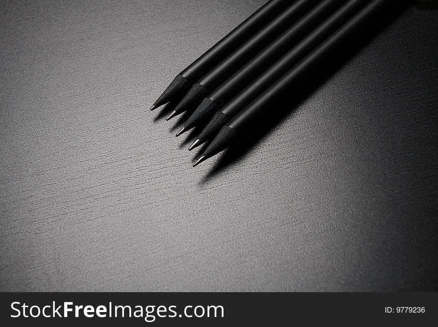 Five black pencils over black leather background