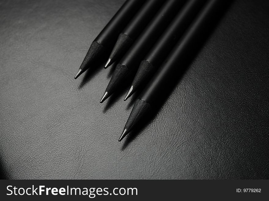 Five black pencils over black leather background