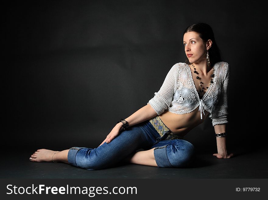 Young slim girl sitting on the floor over black background