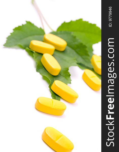 Yellow vitamin pills over green leaves