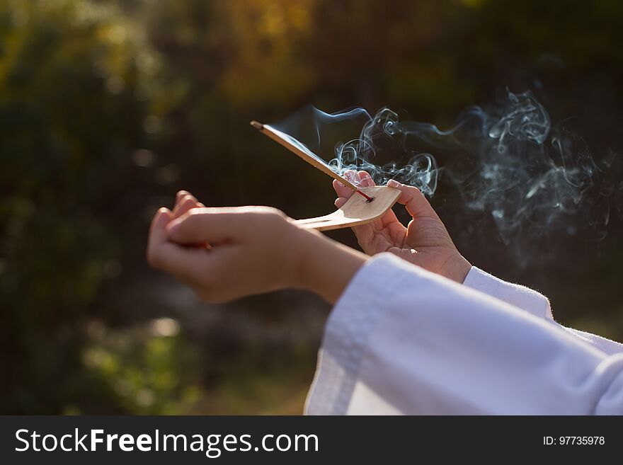 A boy in a kimono holds a burning incense stick, performing a mysterious rite. Sports, meditation, concentration, religion