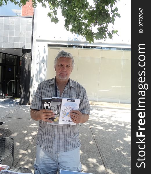Journalist Nebojsa Knevic holds up three of the books he authored, 2017 08 09