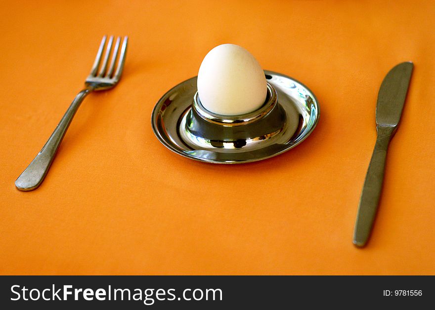Egg, holder, fork and knife over brown tablecloth. Egg, holder, fork and knife over brown tablecloth