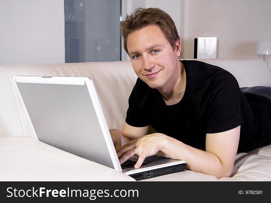 Man using a laptop in the livingroom on a sofa. Man using a laptop in the livingroom on a sofa