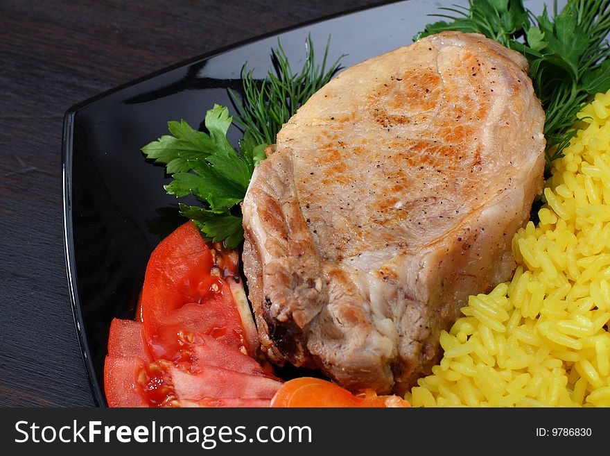 Roasted meat with vegetables and rice on black plate