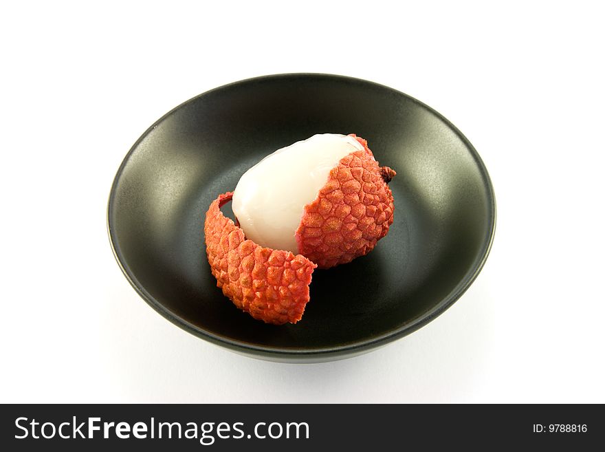 Single peeled lychee in a black dish with clipping on a white background