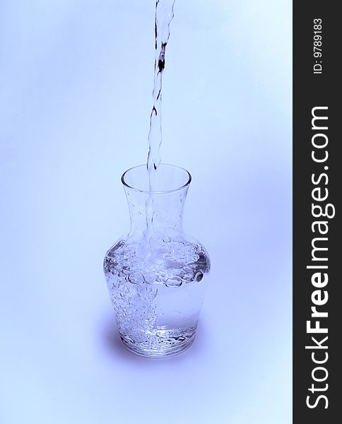 View of water being poured into a glass carafe on a blue background. View of water being poured into a glass carafe on a blue background