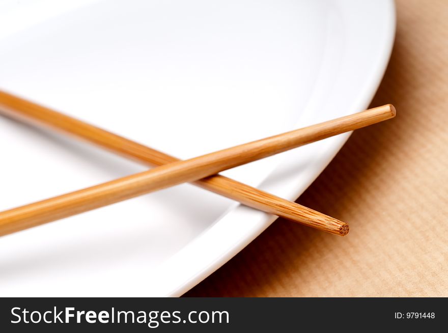 A tilted horizontal macro of a pair of chopsticks on a white plate