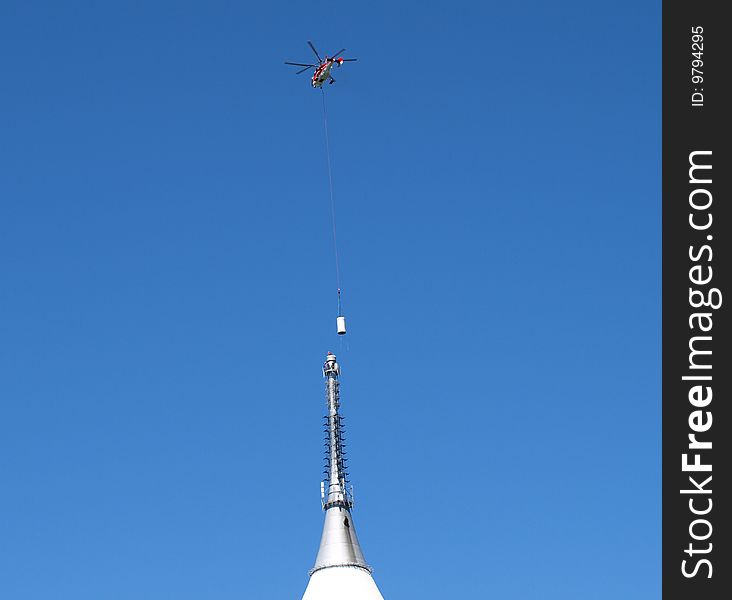 The helicopter settles on top of a television antenna towers new part. The helicopter settles on top of a television antenna towers new part.
