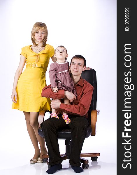 The child sits in an office chair. Mother is beside the child, dad is sitting with a daughter.