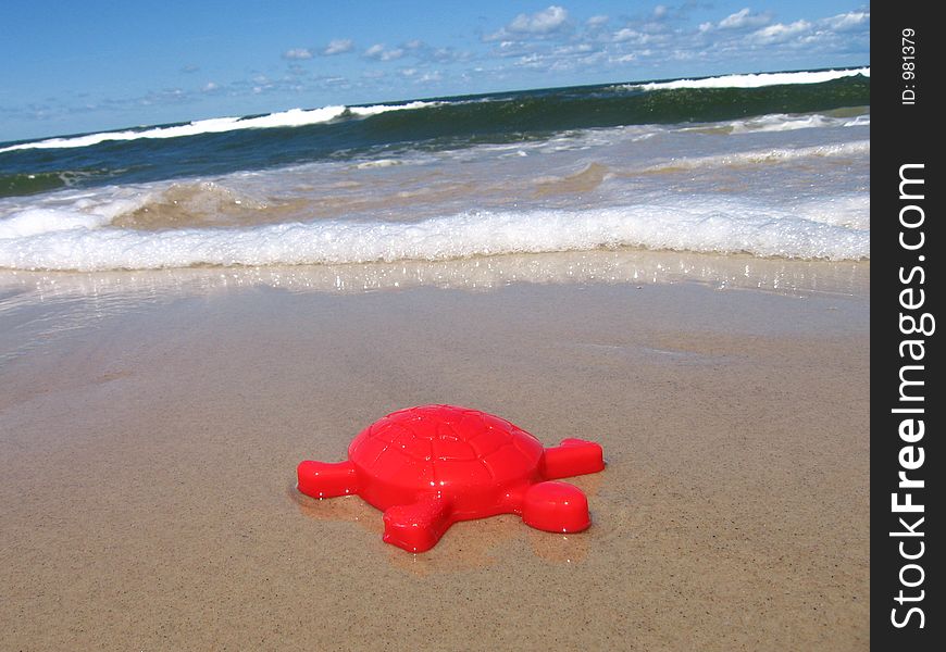 Red turtle's toy in the sand near sea. Red turtle's toy in the sand near sea
