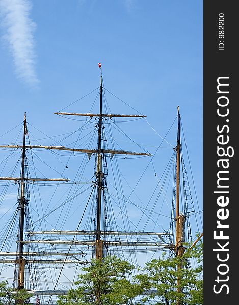 A set of three masts from a tall ship rise above the trees. A set of three masts from a tall ship rise above the trees