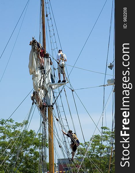 A small group of deckhands climb the lines and work on sails of a tall ship. A small group of deckhands climb the lines and work on sails of a tall ship