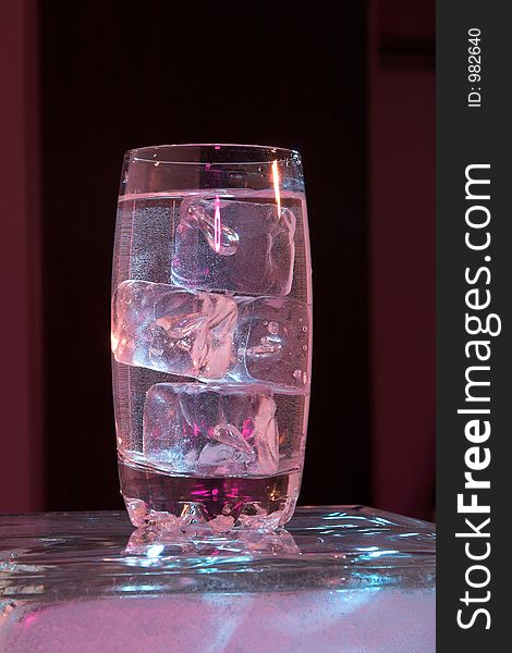 Glass of water with ice lit by purple light