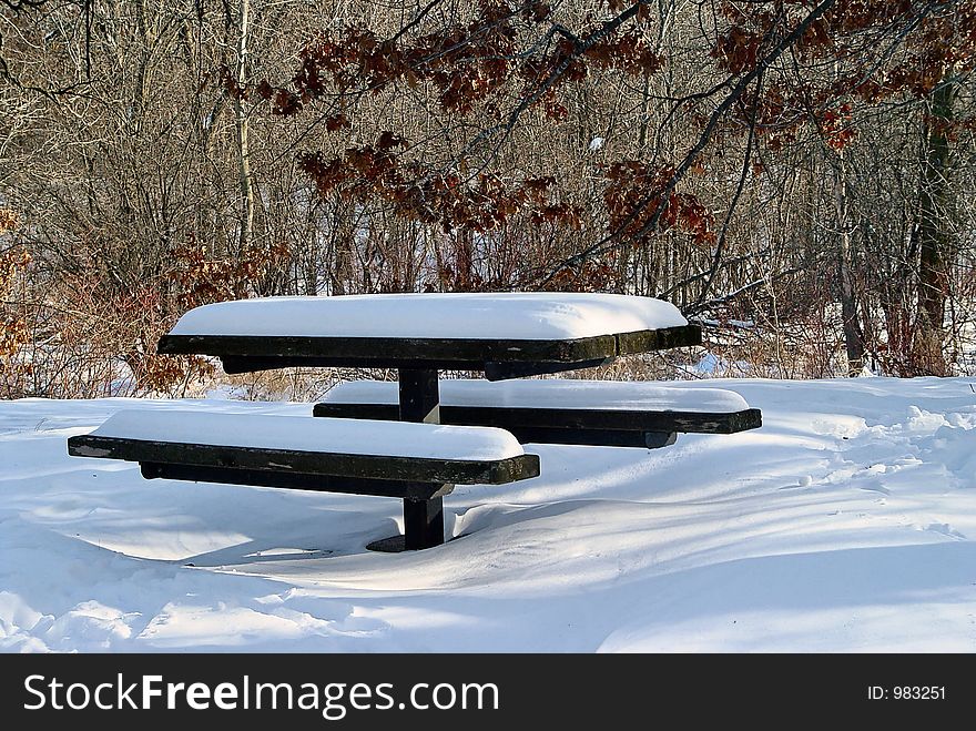 Picnic table covered with a foot of snow in a forest setting. Picnic table covered with a foot of snow in a forest setting.