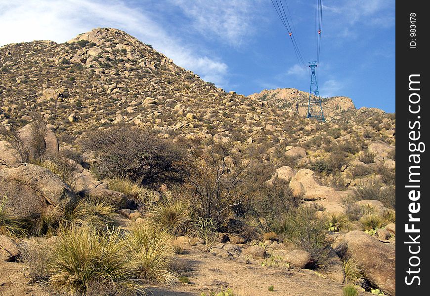Photo of base of Sandia Mountain near Albuquerque New Mexico. The lines and tower for the cable car which takes people to the top of the mountain can be seen on the right. Photo of base of Sandia Mountain near Albuquerque New Mexico. The lines and tower for the cable car which takes people to the top of the mountain can be seen on the right.