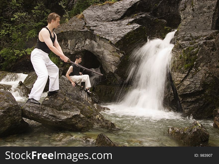 Two young man training their swordsman skills next to waterfall. Two young man training their swordsman skills next to waterfall