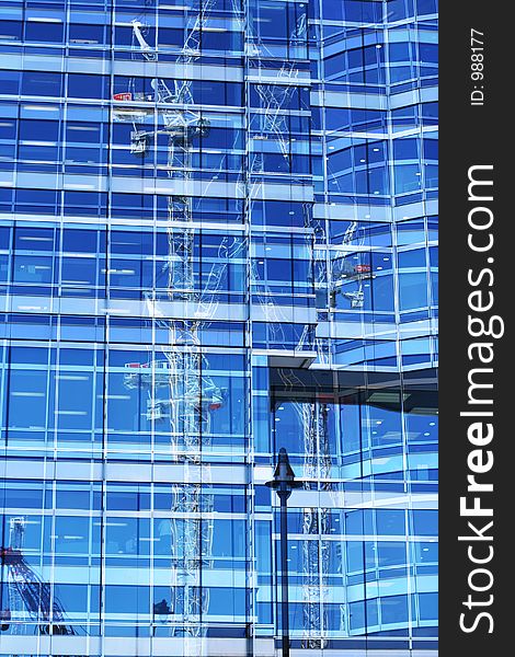Cranes reflected in mirrored office block in docklands london. Cranes reflected in mirrored office block in docklands london