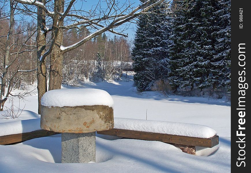 Stone table and a bench covered by snow near frozen river. Stone table and a bench covered by snow near frozen river