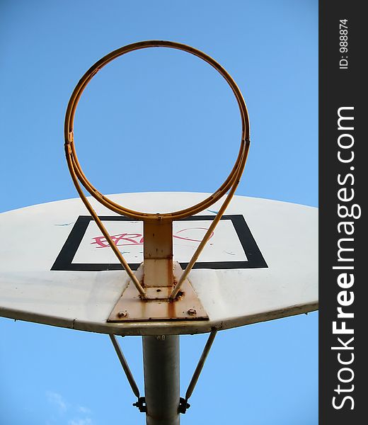 A basketball hoop without the basket netting. Graffiti was sprayed on the board. Focused at the ring.