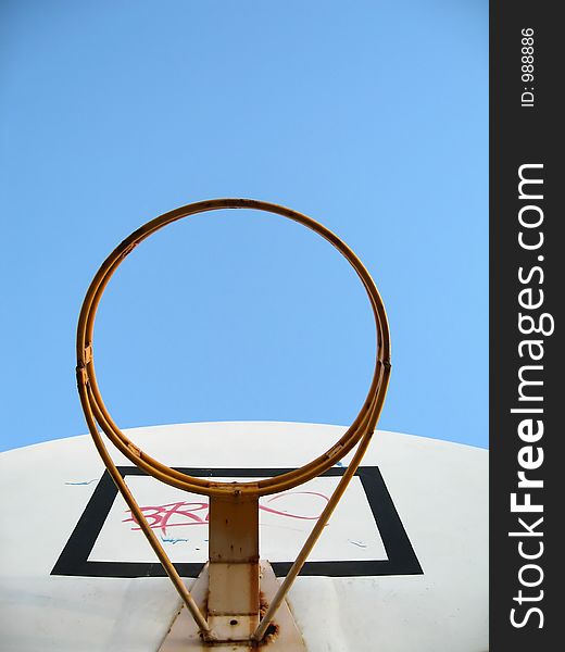 A basketball hoop without the basket netting. Graffiti was sprayed on the board. Focused at the ring.