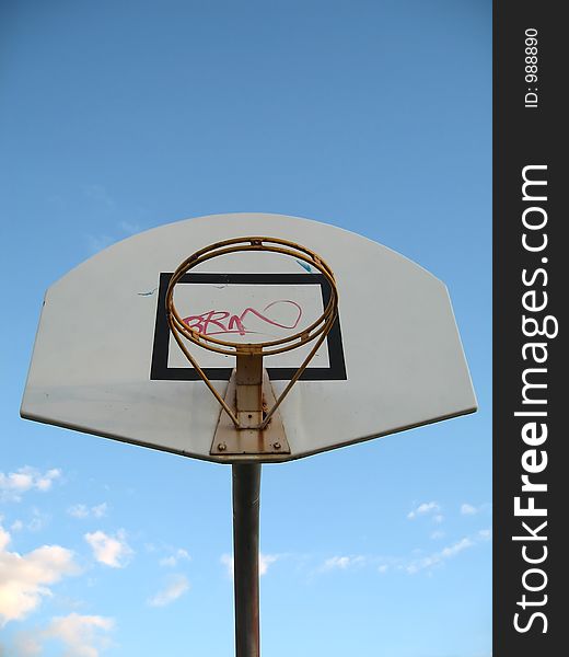 A basketball hoop without the basket netting. Graffiti was sprayed on the board. Focused at the ring.