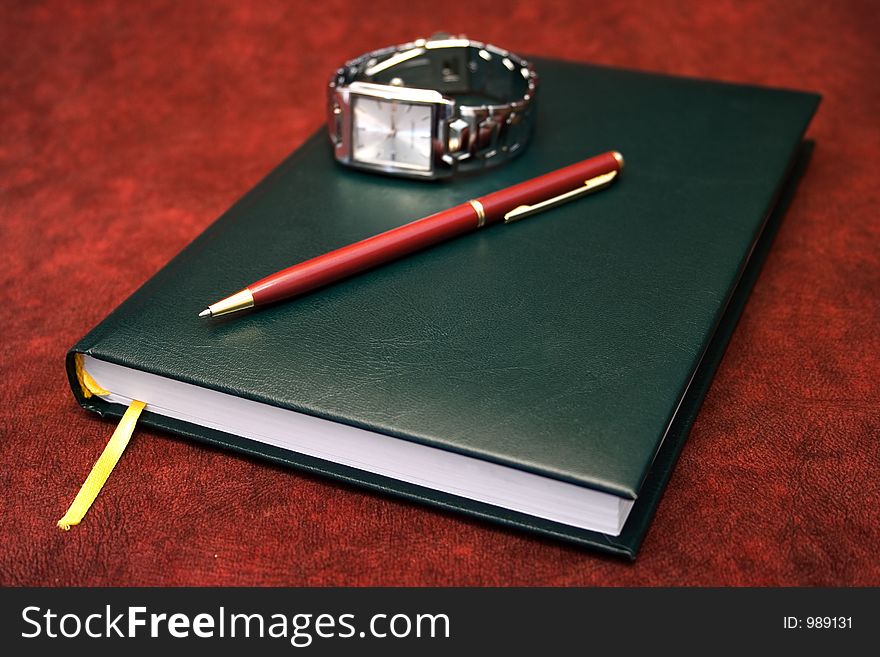 A green agenda under a red pen and a wrist watch, useful in business designs. A green agenda under a red pen and a wrist watch, useful in business designs