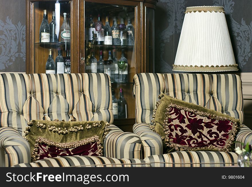 Interior of a retro, vintage room with two armchairs with cushions and cabinet with wine bottles behind. Interior of a retro, vintage room with two armchairs with cushions and cabinet with wine bottles behind.