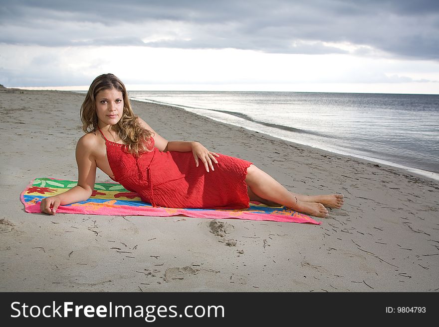 Attractive girl laying on a towel with red dress, at beach sunset