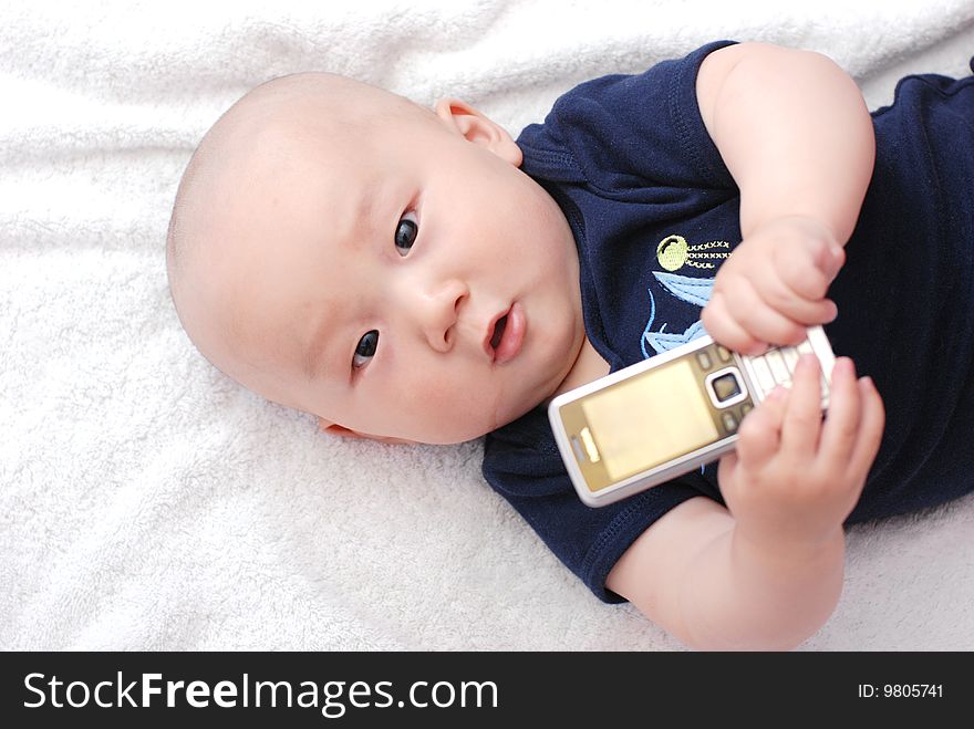 Cute little baby boy holding a cellphone on bed. Cute little baby boy holding a cellphone on bed