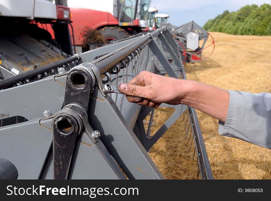 Man's hand reapiring harvester whith wrench on field