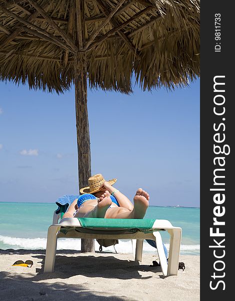 Woman laying on deckchair under wood umbrella over blue sea and blue sky. Woman laying on deckchair under wood umbrella over blue sea and blue sky