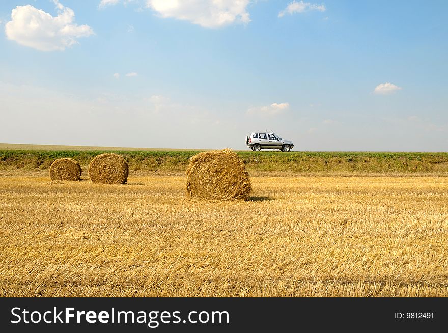 Field with three rolls of straw and car on horizont line