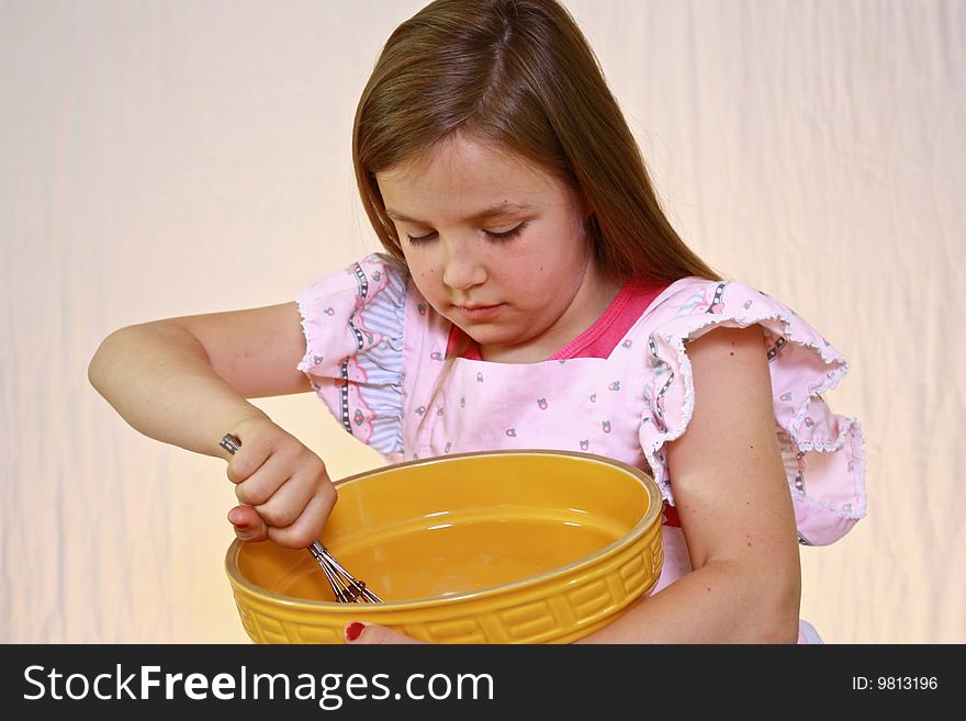Young cute girl with pink apron and mixing bowl.